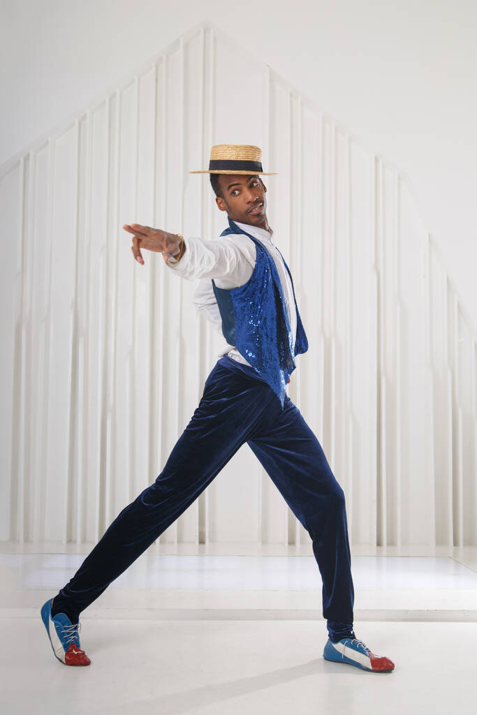 Een zwarte man in podiumkleren danst in een heldere kamer.. - Foto, afbeelding