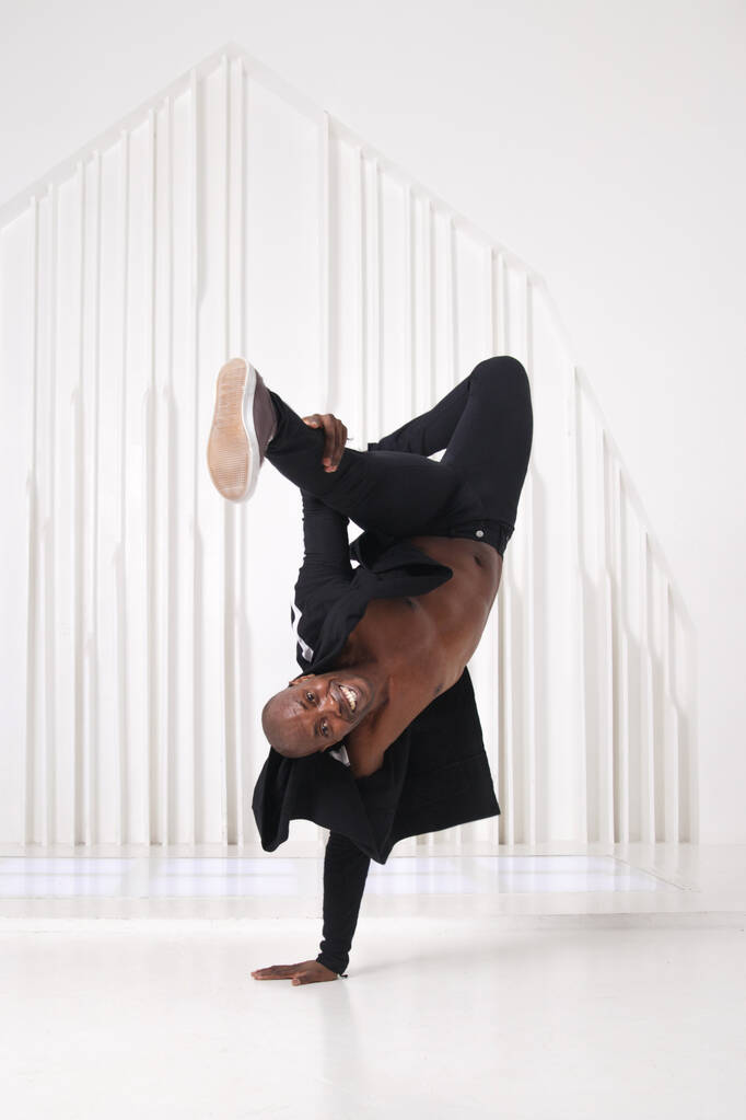 Elegante homem negro dançarino em roupas pretas faz um suporte de mão em um quarto brilhante. - Foto, Imagem