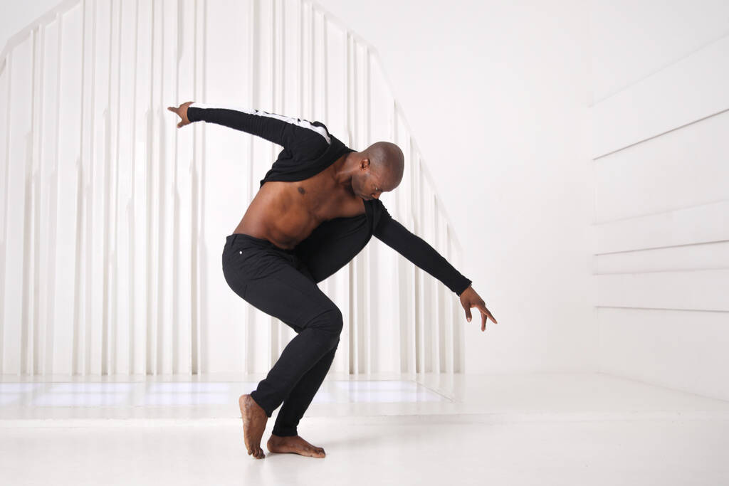 Elegante zwarte man danser in zwarte kleren danst in een lichte kamer. - Foto, afbeelding