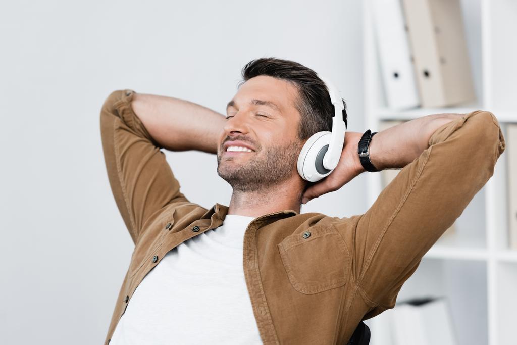 Empresário sorridente em fones de ouvido relaxante enquanto ouve música no fundo embaçado - Foto, Imagem