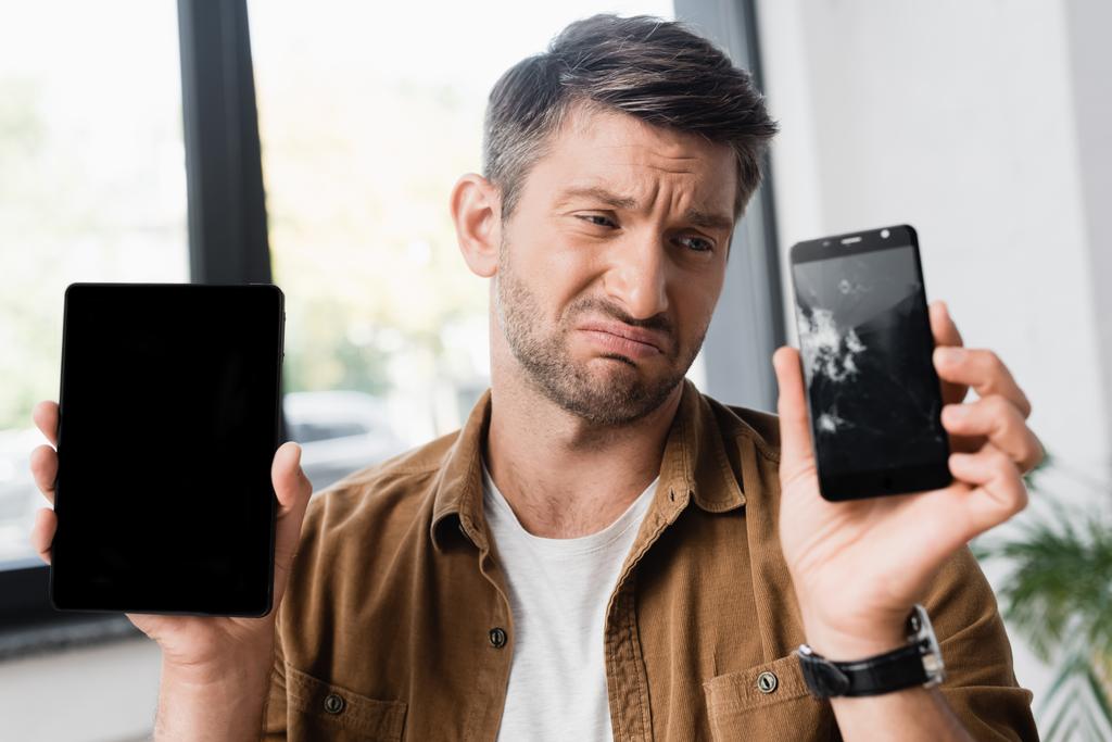 Сумний бізнесмен тримає смартфон з порожнім екраном, дивлячись на розбитий мобільний телефон на розмитому фоні
 - Фото, зображення