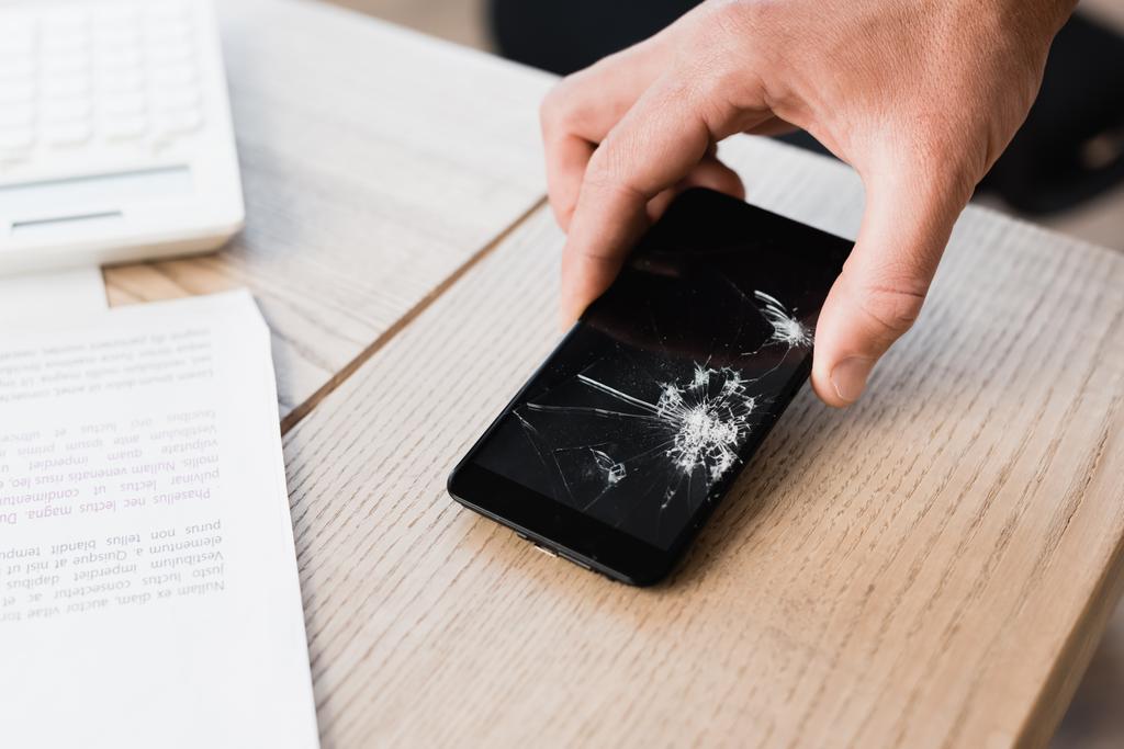 Oříznutý pohled na člověka, jak dává rozbitý smartphone na stůl na rozmazaném pozadí - Fotografie, Obrázek