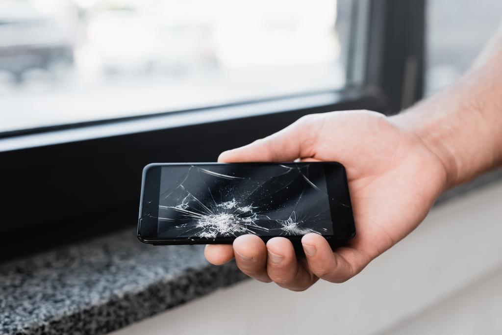 Обрізаний вид бізнесмена, що тримає розбитий смартфон на розмитому фоні
 - Фото, зображення