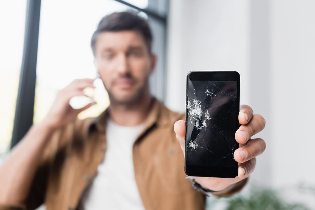 Smashed smartphone in hand of businessman on blurred background - Photo, Image