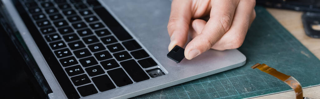 Cropped view of repairman holding broken key of keyboard near laptop at workplace, banner - Photo, Image