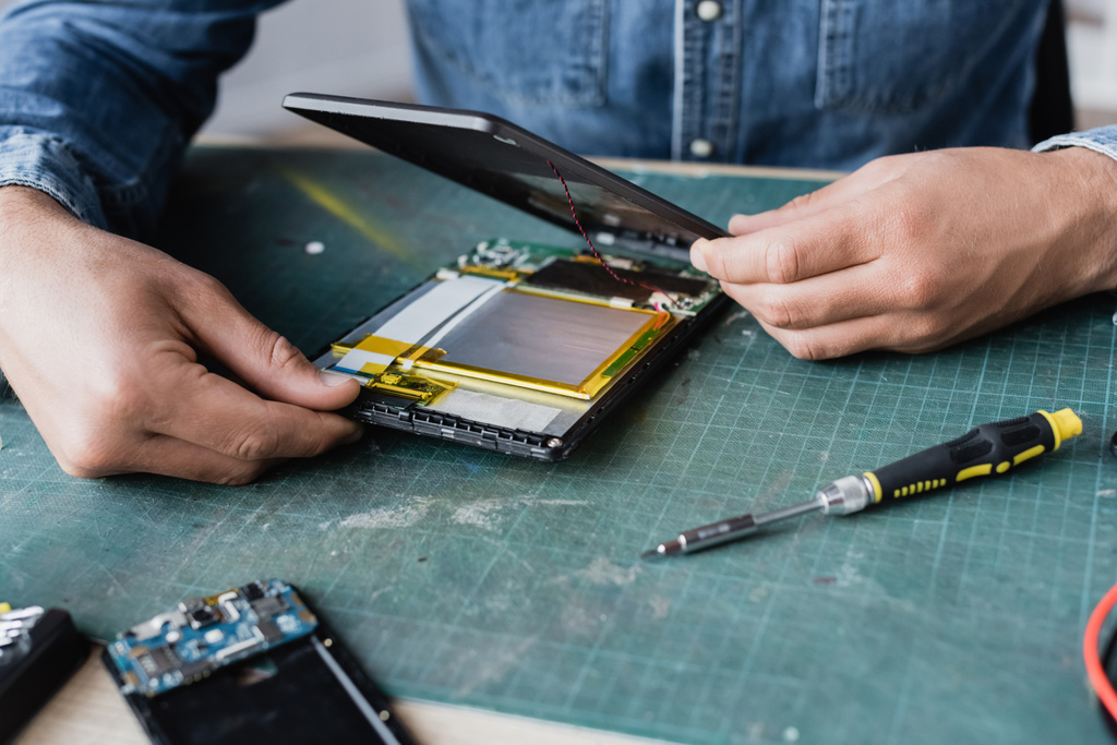Nahaufnahme von Reparaturhänden beim Demontieren eines kaputten digitalen Tablets in der Nähe eines Schraubendrehers am Arbeitsplatz - Foto, Bild