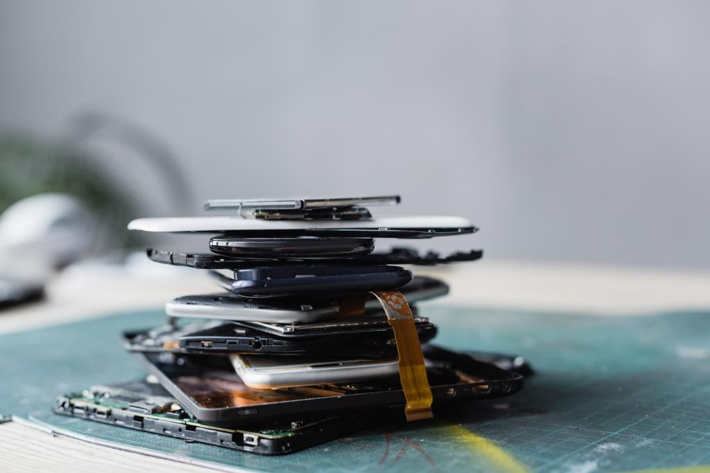 Nahaufnahme eines Haufens mit zerlegten Mobiltelefonen und Batterien mit verschwommenem Arbeitsplatz im Hintergrund - Foto, Bild