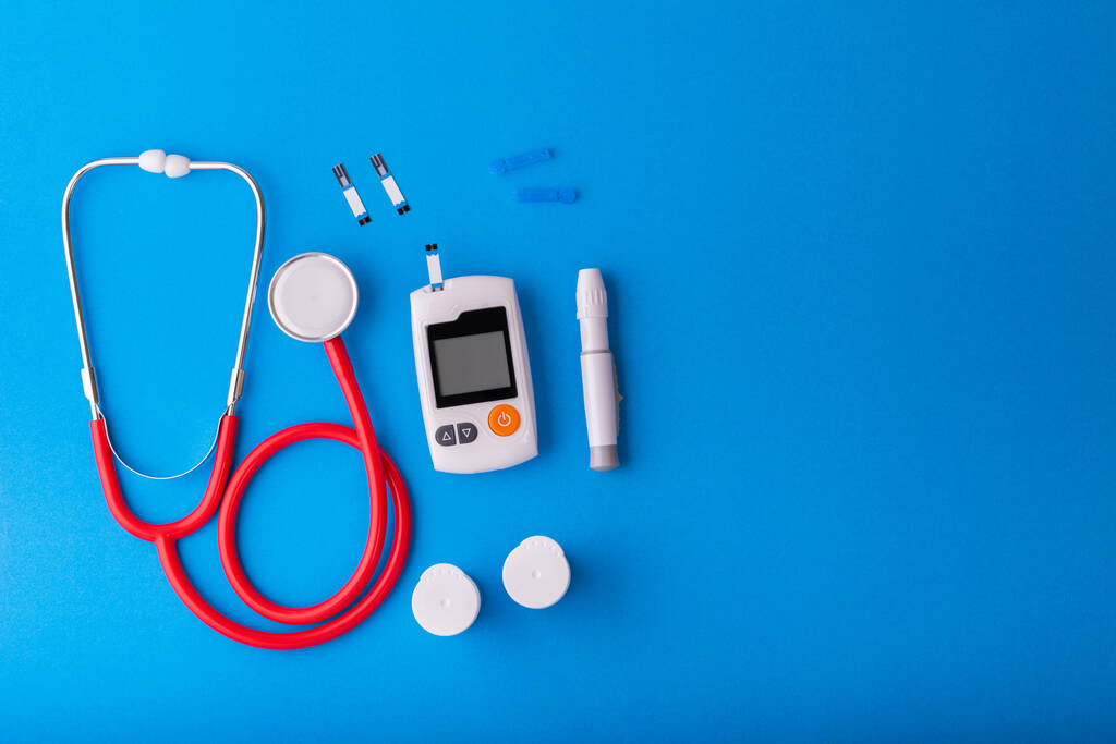 世界糖尿病の日,青い背景に無料のグルコースモニターと赤い聴診器は、上のビューに青に置きます｜健康と医療の概念 - 写真・画像