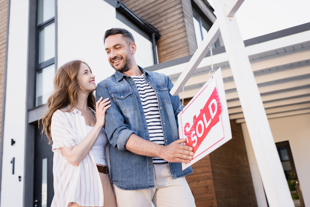 Couple souriant se regardant près signe avec lettrage vendu près de la maison - Photo, image