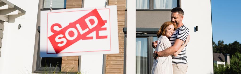 Casal sorridente abraçando enquanto está perto do sinal com letras vendidas em primeiro plano desfocado, banner - Foto, Imagem