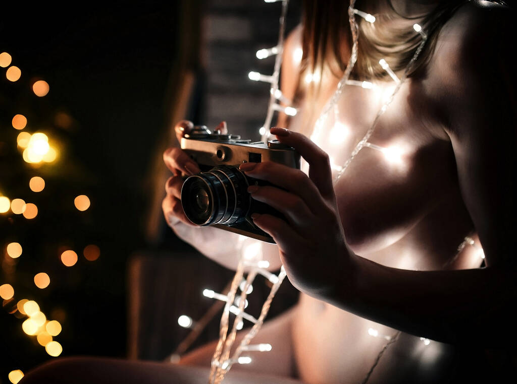 Beautiful sexy model with a glowing garland. Young naked woman holding a vintage camera - Photo, Image