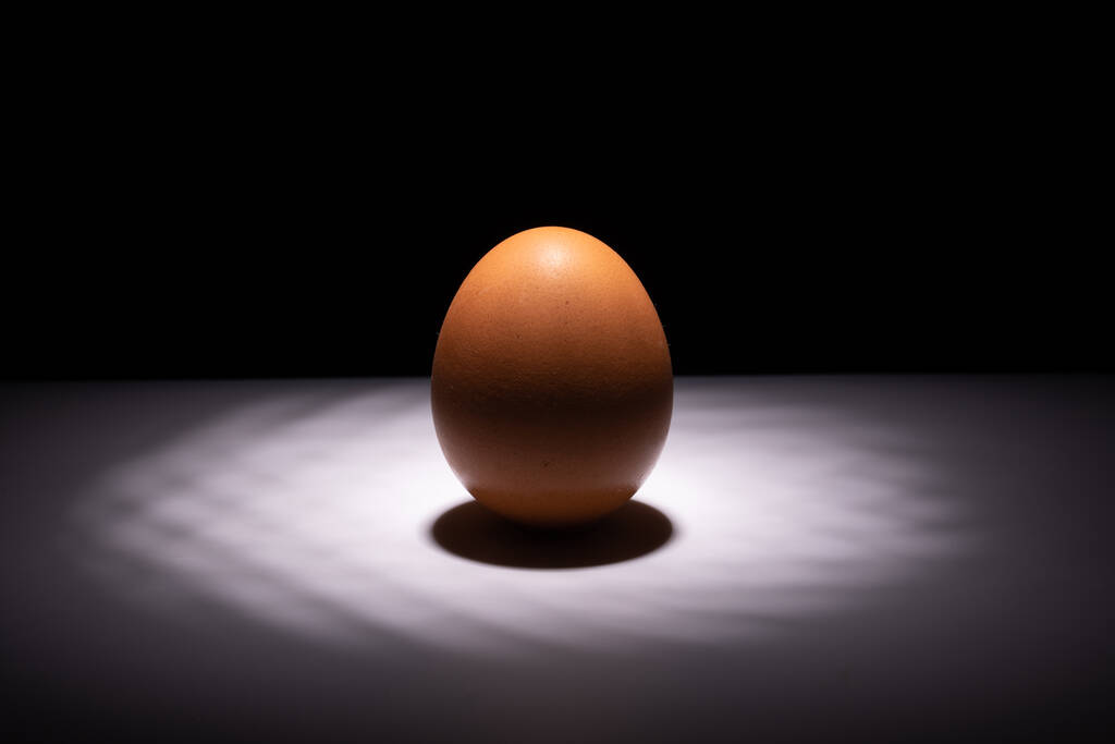 Ei steht auf dem Tisch, beleuchtet von einem Scheinwerfer von oben in verschiedenen Farben - Foto, Bild