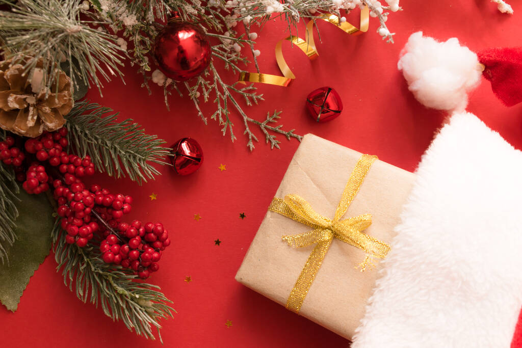 Krásná vánoční kompozice s dárkovou krabicí svázaná stuhou, dárky, Santa klobouk a jedle větve na červeném pozadí. - Fotografie, Obrázek
