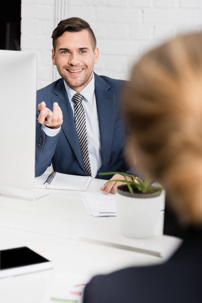 Cheerful businessman gesturing, while sitting at table with blurred female colleague on foreground - Photo, Image