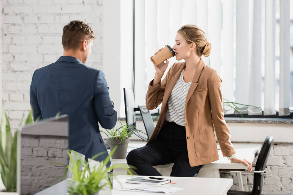 Вид ззаду бізнесмена, що стоїть біля жінки-колегині, п'є каву під час перерви в офісі
 - Фото, зображення