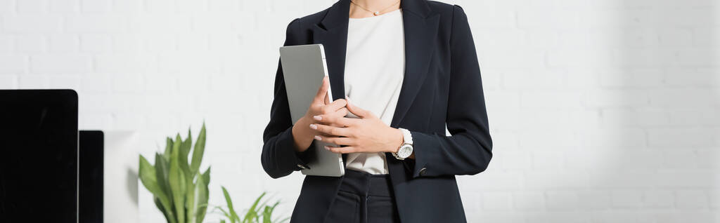 Vista recortada de la mujer de negocios en ropa formal que sostiene el ordenador portátil cerca de las plantas y monitores de ordenador, pancarta - Foto, Imagen