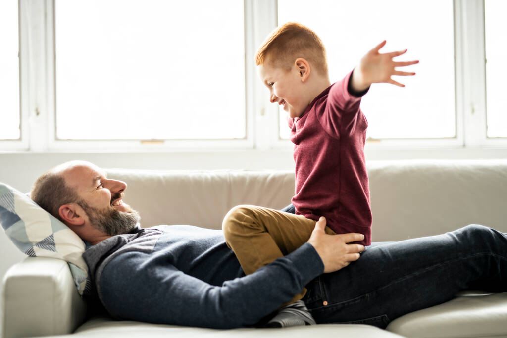 Vater mit rothaarigem Kind amüsiert sich zu Hause auf dem Sofa - Foto, Bild