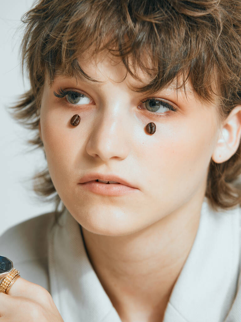 Kaffeebohnen auf jungem Mädchengesicht wie Tropfen, stylischer Kurzhaarschnitt, weibliches Nahaufnahme-Studioporträt - Foto, Bild
