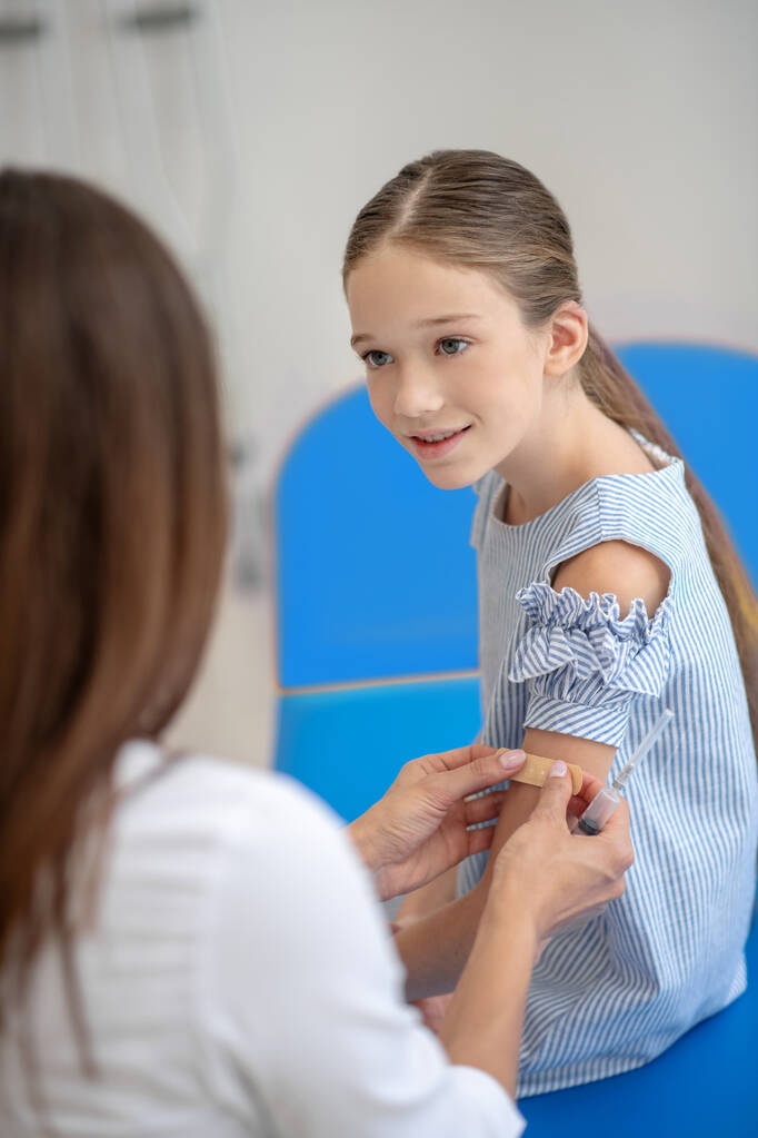 Médico sosteniendo el brazo de las niñas y aplicando un yeso después de la vacunación - Foto, imagen