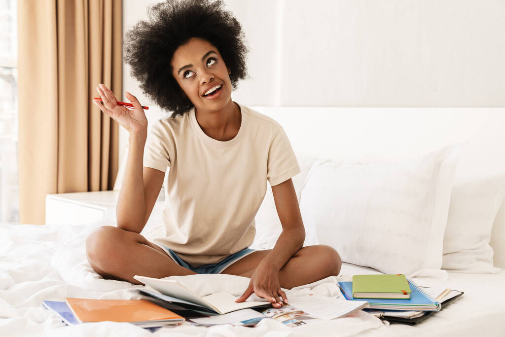 Image of young cheerful african american girl smiling while doing homework on bad - Photo, Image