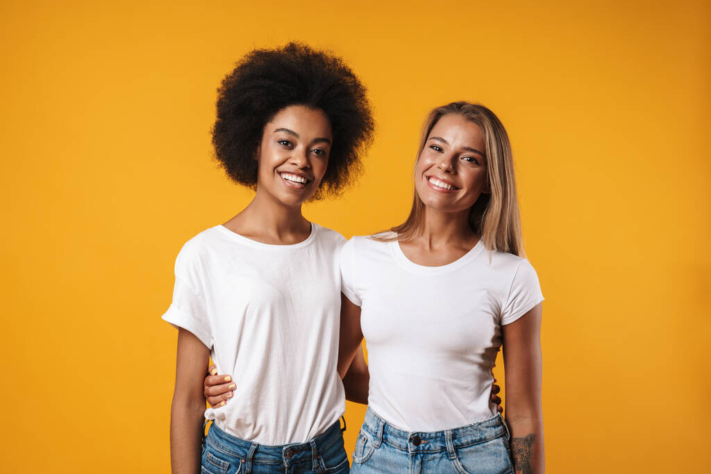 Зображення веселих позитивних молодих багаторасових дівчат друзів позують ізольовані на жовтому фоні стіни
 - Фото, зображення