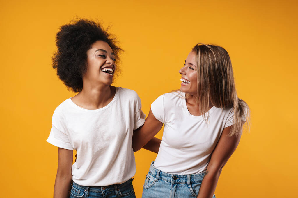 Afbeelding van een vrolijke positieve jonge multiraciale meisjes vrienden poseren geïsoleerd over gele muur achtergrond - Foto, afbeelding