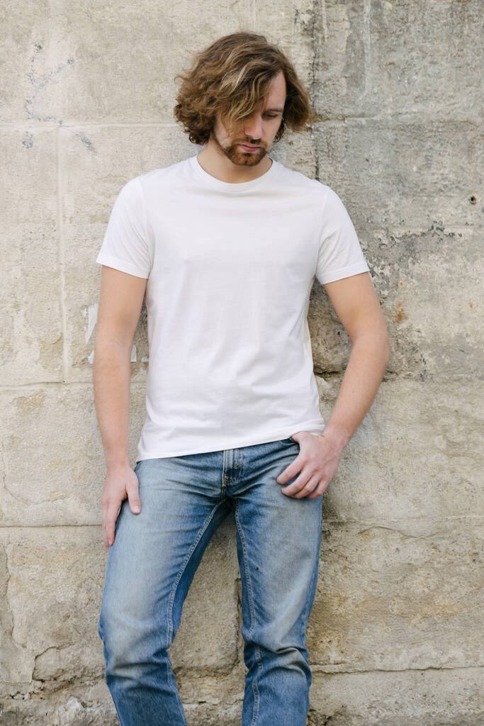Hipster όμορφο ανδρικό μοντέλο φορώντας λευκό κενό t-shirt με χώρο για το λογότυπο ή το σχέδιό σας σε casual αστικό στυλ στις ευρωπαικές οδούς - Φωτογραφία, εικόνα