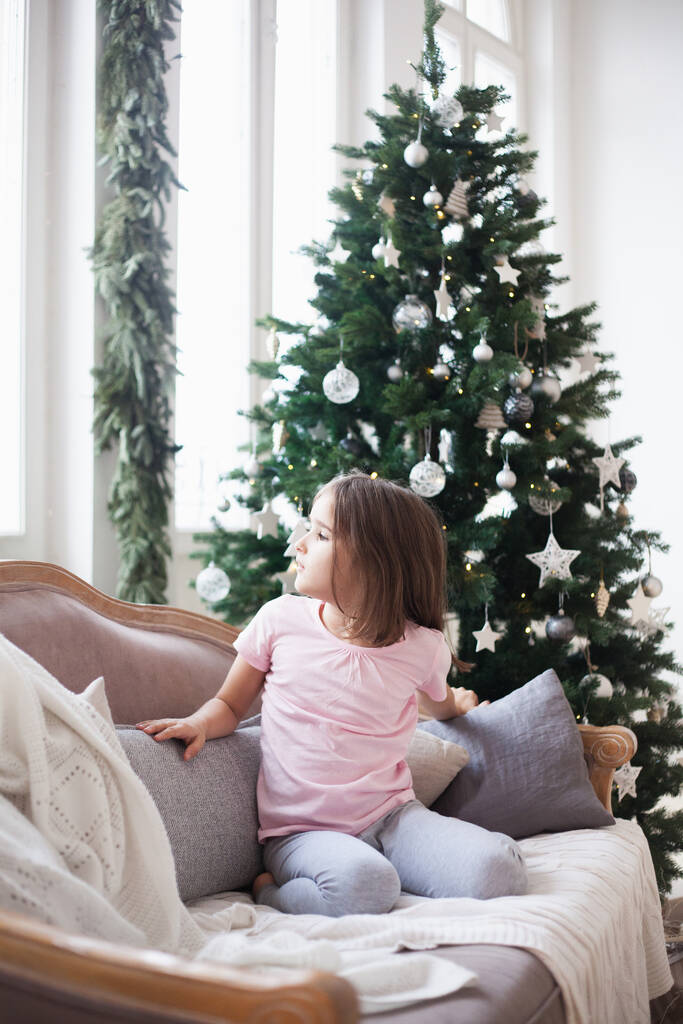 A szoba díszített az új évre, egy lány a kanapén várja az ajándékokat, karácsony reggel - Fotó, kép