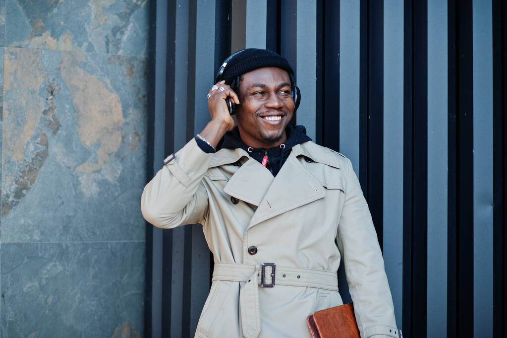 Hombre afroamericano con auriculares, usar en sombrero y abrigo escuchando música sobre fondo de acero. - Foto, imagen