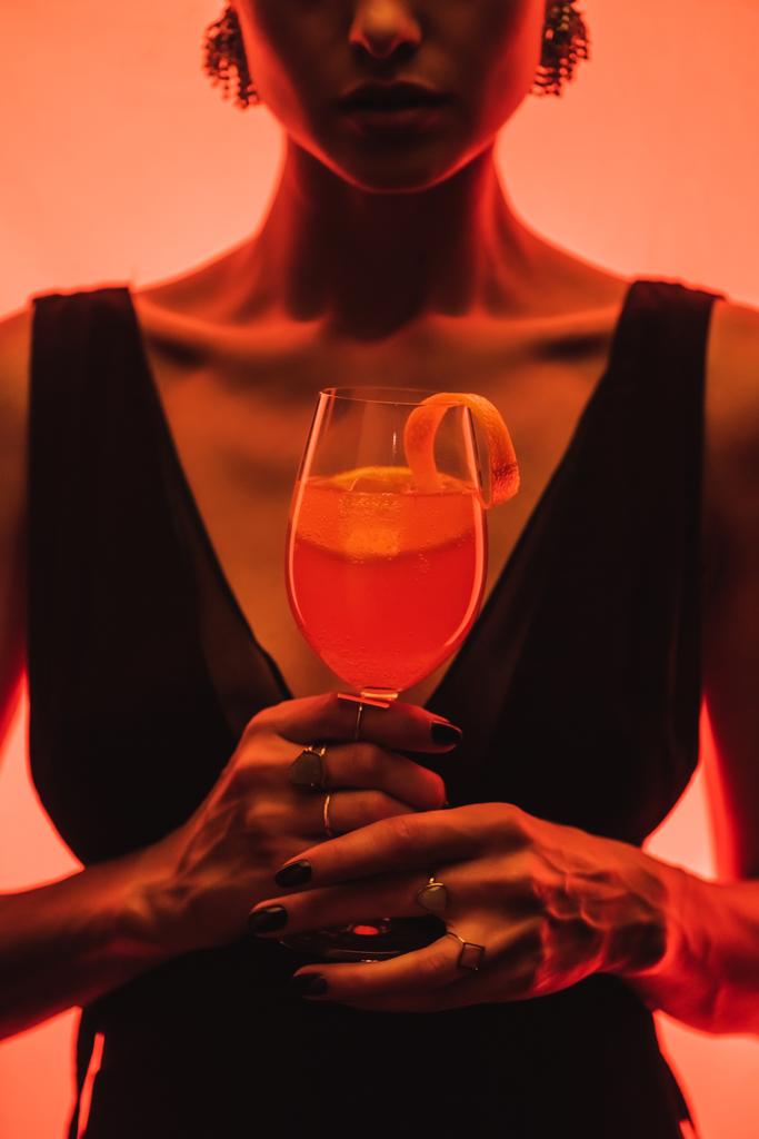 cropped view of elegant woman holding glass with mixed cocktail and orange on pink  - Photo, Image