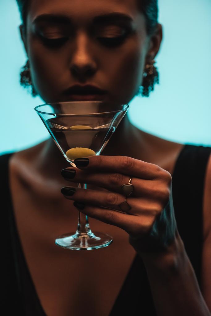 vaso de martini con oliva en mano de mujer sobre fondo borroso aislado sobre azul - Foto, imagen