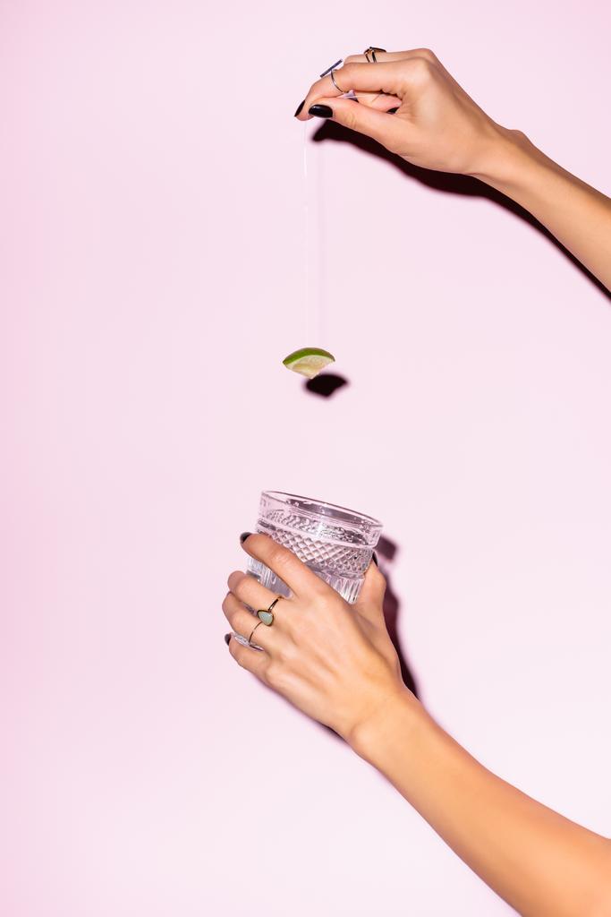 vista recortada de la mujer sosteniendo cal por encima del vidrio con bebida alcohólica en rosa - Foto, imagen