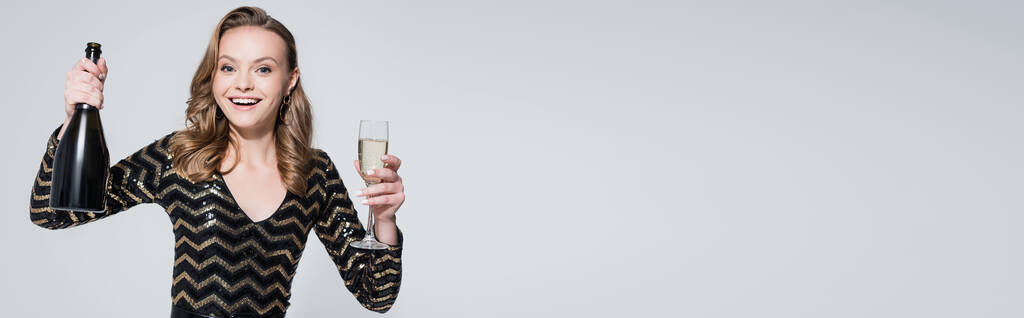 vidám nő kezében üveg pezsgő és üveg elszigetelt szürke, banner - Fotó, kép