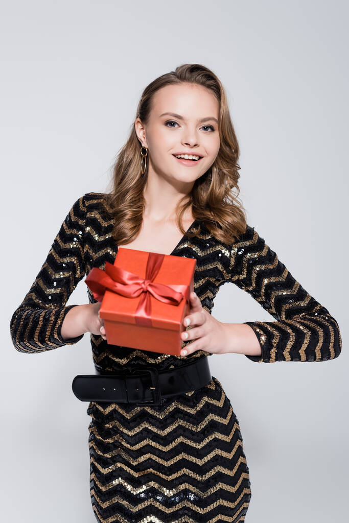 mladá veselá žena držící vánoční dárek izolované na šedé  - Fotografie, Obrázek