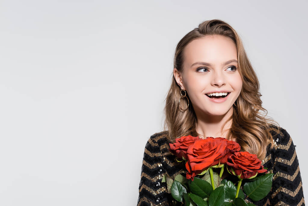 excited young woman holding bouquet of red roses isolated on grey - Photo, Image