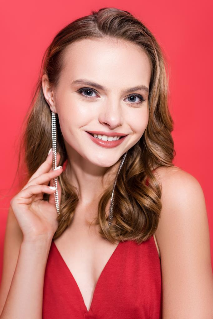 fröhliche junge Frau mit Ohrringen, die auf Rot lächelt  - Foto, Bild
