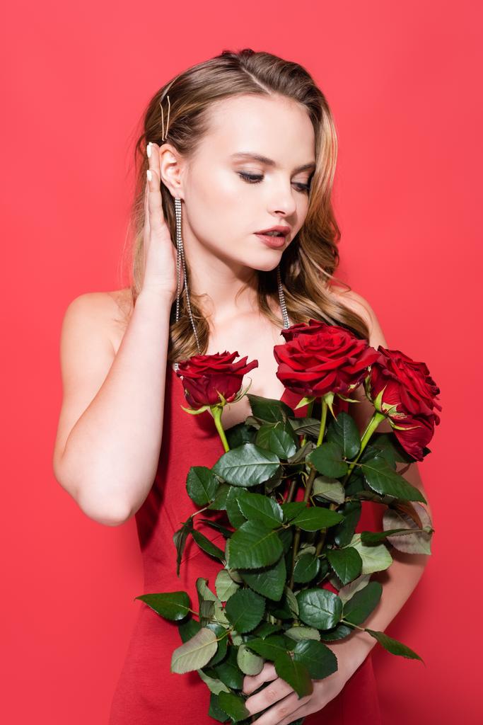 giovane donna che guarda le rose e fissa i capelli sul rosso  - Foto, immagini