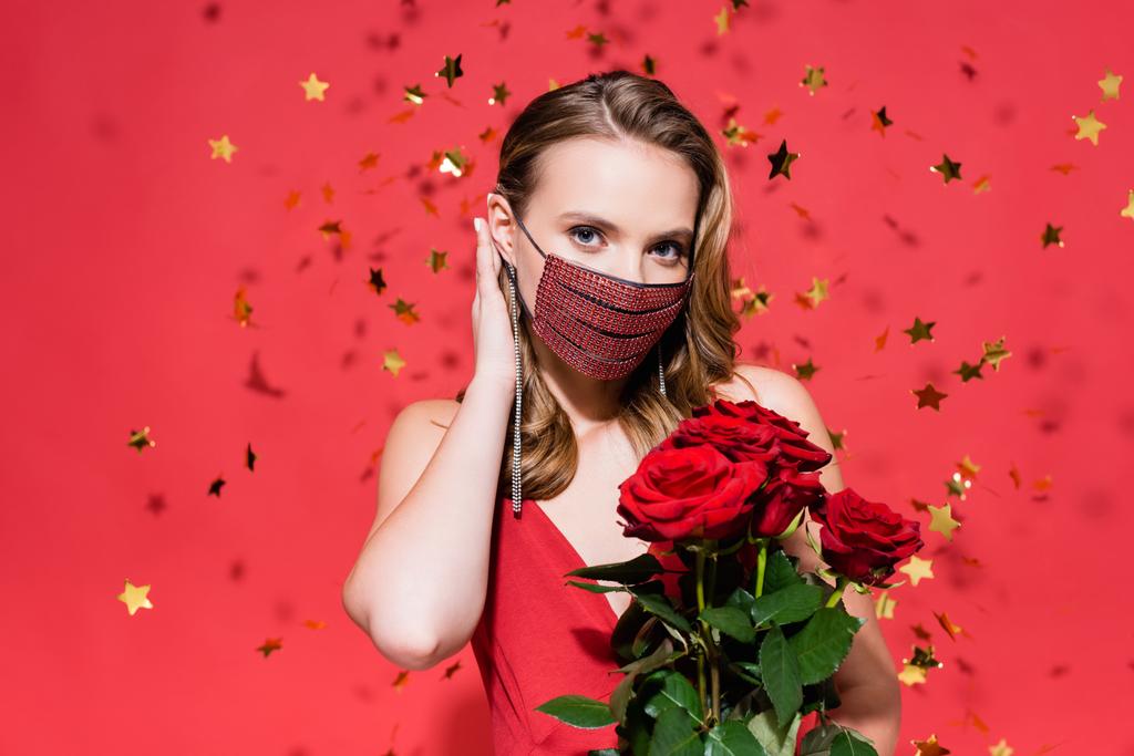 Nainen suojaava naamio strassit vahvistamisesta hiukset lähellä ruusuja ja konfetti punainen - Valokuva, kuva
