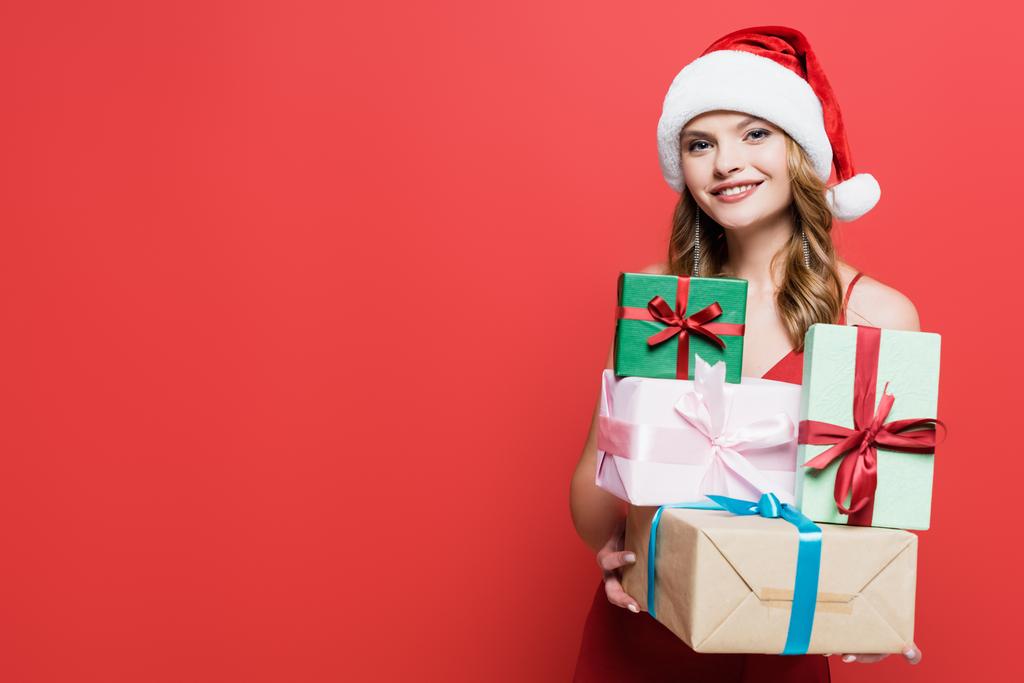 fröhliche Frau mit Weihnachtsmütze und Geschenkschachteln auf rotem Grund - Foto, Bild