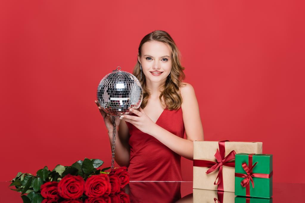 radostná žena drží diskotéka míč v blízkosti vánočních dárky a růže na červené - Fotografie, Obrázek