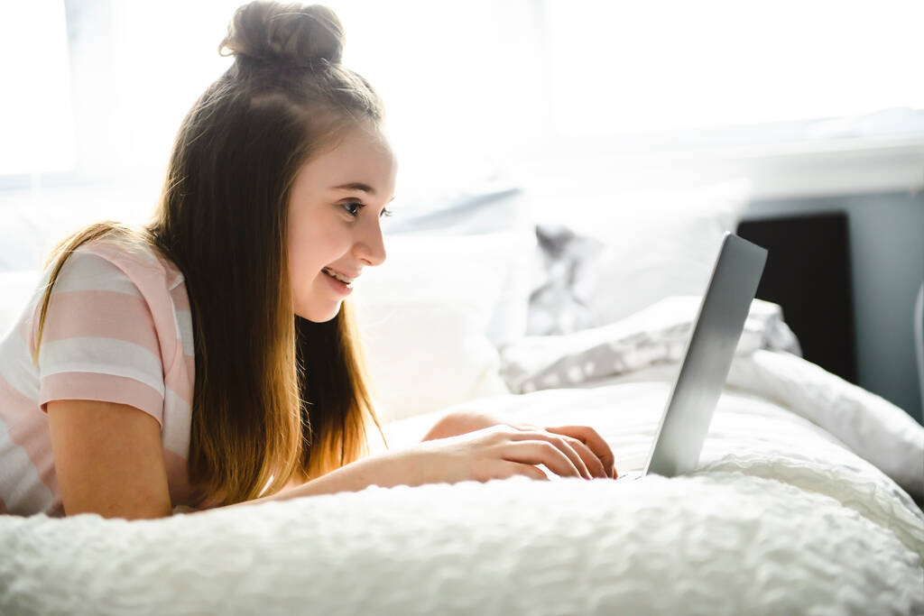 Una giovane ragazza sorridente sul letto con il computer portatile - Foto, immagini