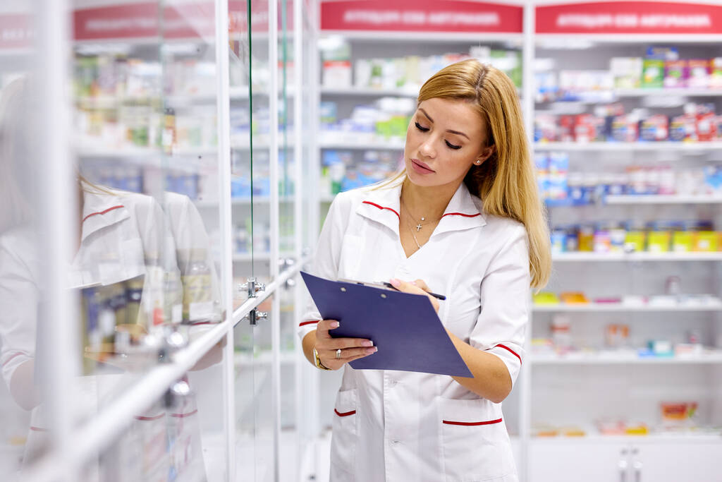 молодая симпатичная женщина-фармацевт ищет лекарства на полках аптек - Фото, изображение