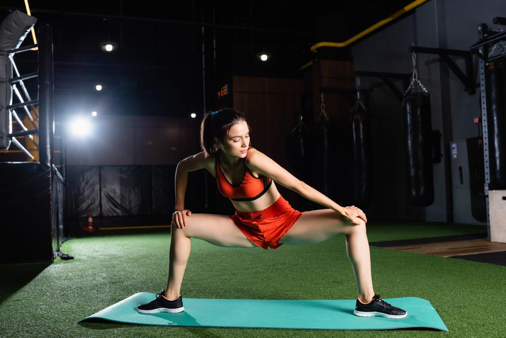 mujer deportiva en pantalones cortos y piernas de estiramiento superior mientras hace ejercicio en el centro deportivo - Foto, imagen