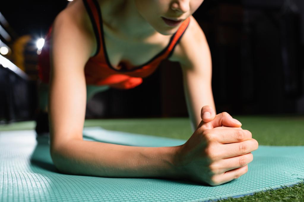 gedeeltelijk zicht op sportvrouw doen plank oefening tijdens de training in de sportschool, wazig achtergrond - Foto, afbeelding
