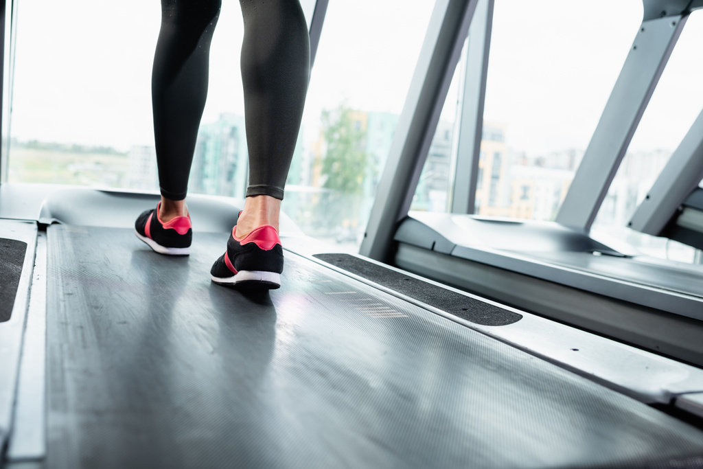 vista recortada de la deportista en leggings y zapatillas de entrenamiento en la cinta de correr - Foto, imagen