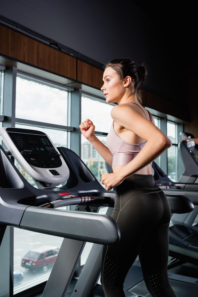 side view of sportswoman in leggings looking away while running on treadmill - Photo, Image