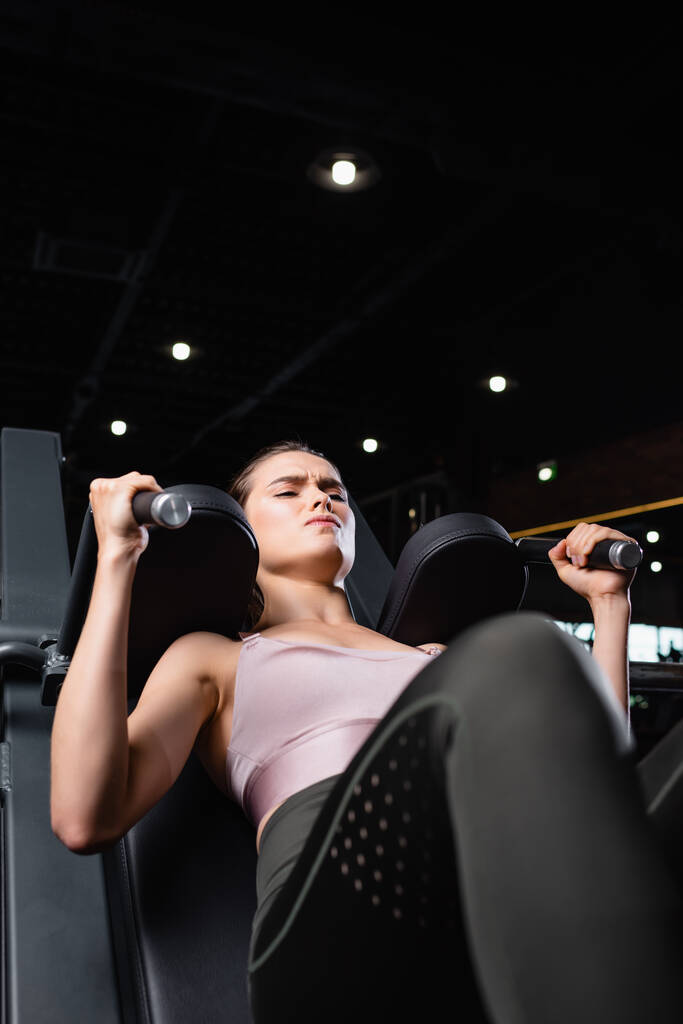 athletic sportswoman doing arms extension exercise on training machine on blurred foreground - Photo, Image
