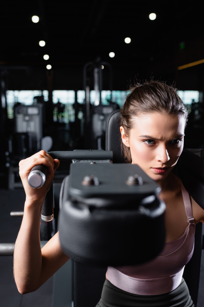 sportive woman doing arms extension exercise on training machine on blurred foreground - Photo, Image