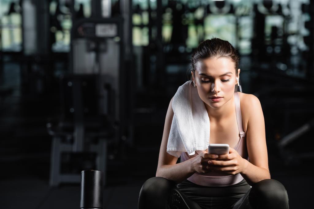 mensajería deportiva en el teléfono móvil mientras está sentado en el gimnasio con toalla en el hombro - Foto, imagen