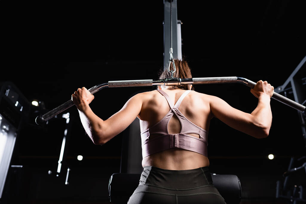 Rückenansicht einer sportlichen Frau bei Arm- und Rückenstreckübungen an einem Latexgerät - Foto, Bild